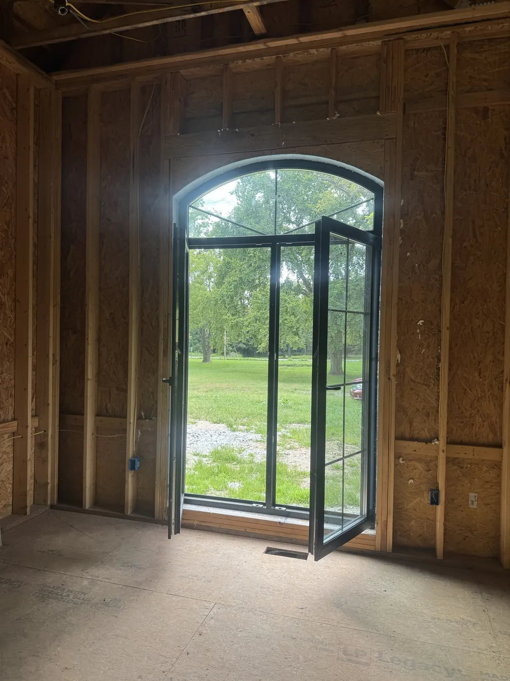 Arched door and transom with black frames, doors open to the lawn